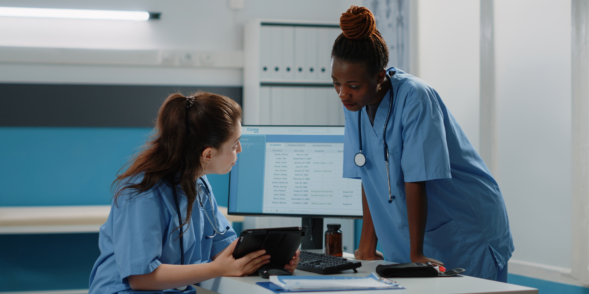 Two women working in healthcare on computer and tablet